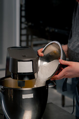 close-up of hands in a professional kitchen over an iron table baker pours sugar into the machine