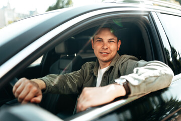 Young smiling man sitting in a car with open window