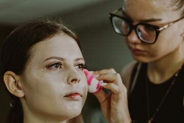 A young makeup artist applies foundation to a girl s face.