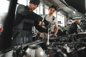 Two male mechanics repairing car in car service