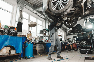 Workman mechanic working under car in auto repair shop - obrazy, fototapety, plakaty