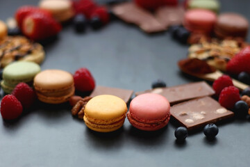 Macarons, chocolate, cookies, berries and various nuts on dark blue background. Selective focus.