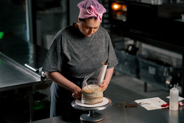female baker in a professional kitchen wraps an almost finished cake in cling film