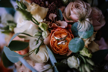 Valmiera, Latvia- July 28, 2024 - Golden wedding bands nestled in a bridal bouquet with roses and...