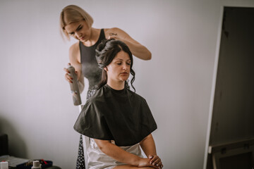 Valmiera, Latvia- July 28, 2024 - A hairstylist is styling a seated woman’s hair, using hairspray.
