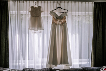 Valmiera, Latvia- July 28, 2024 - Two elegant dresses hanging by a window, lit by natural light.