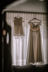 Valmiera, Latvia- July 28, 2024 - Two elegant dresses hanging by a window, lit by natural light.