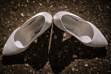 Valmiera, Latvia- July 28, 2024 - A pair of white bridal shoes on a textured surface with a pebble...