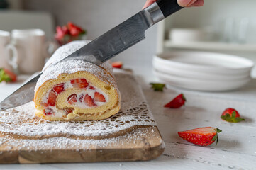 Fresh baked cake roll or cake roulade is getting cut by woman´s hand with a kitchen knife