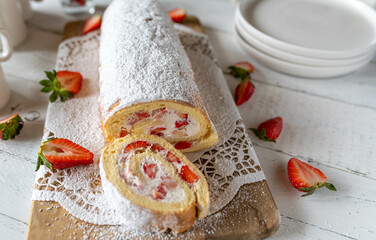 Swiss roll or cake roulade with whipped cream and strawberry filling on white table background