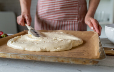 Woman spreading batter with a dough scraper on a baking sheet. Making a sponge cake base
