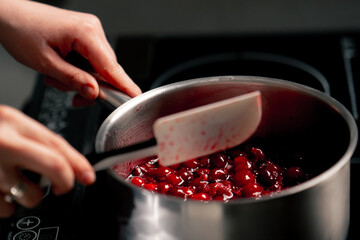 close-up in a professional kitchen mixing cherries with a spatula in a saucepan for jam
