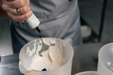 close-up of a female baker in a professional kitchen adding blue coloring to white cream