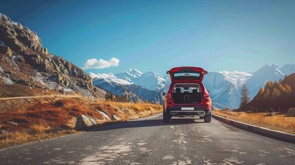 A red SUV with an open trunk stands on the edge of an alpine mountain, with a panoramic view of the mountains and a blue sky with clouds.