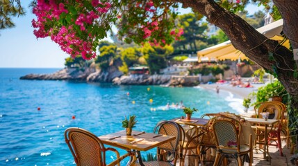 Authentic atmospheric cafe on the shore of the French Riviera under green trees overlooking clear blue water, colorful flowers in the background - obrazy, fototapety, plakaty