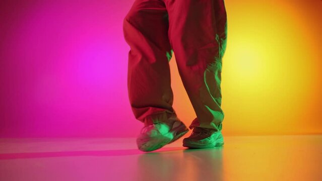 Cool attitude young, man performing breakdance steps in motion in neon light against gradient pink-yellow background. Concept of art, hobby, sport, creativity, fashion and style, action. Ad