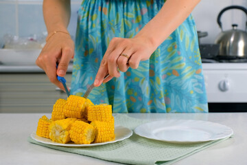Woman cutting piece of baked corn on plate on kitchen at home to eat, hand close-up. Prepare cook bake dish. Cuisine culinary nutrition domestic food recipe ingredients vegetable. Cooked sweet corn.