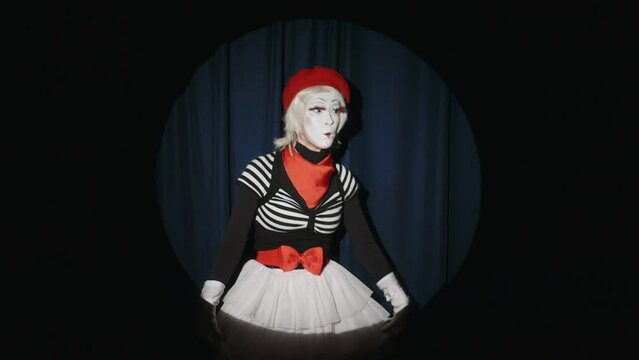 Surprised mime artist standing in spotlight on theatre stage, looking at audience, waving and smiling in beginning of comedy performance