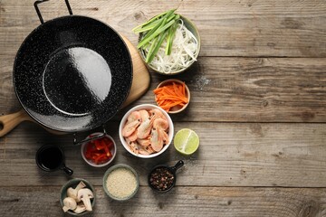 Flat lay composition with black wok, spices and products on wooden table. Space for text