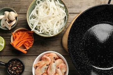 Flat lay composition with black wok, spices and products on wooden table