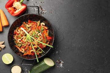 Shrimp stir fry with vegetables in wok and ingredients on black table, flat lay. Space for text