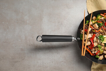 Stir-fry. Tasty noodles with meat in wok and chopsticks on grey textured table, top view. Space for...