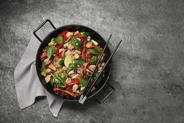 Stir-fry. Tasty noodles with meat in wok and chopsticks on grey textured table, top view. Space for text