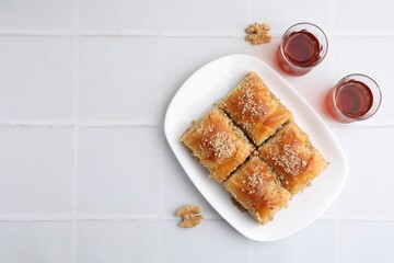 Eastern sweets. Pieces of tasty baklava, walnuts and tea on white tiled table, flat lay. Space for text