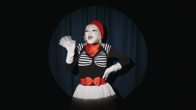 Cheerful female mime artist jumping out in spotlight on stage, waving and smiling on camera while greeting audience in beginning of comedy show
