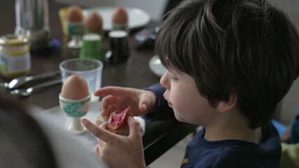 Back of little boy eating toast with jelly seated at breakfast table, close-up of 5 year old boy...
