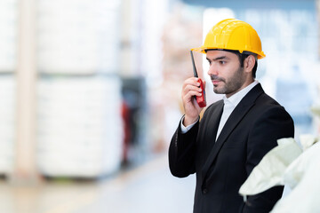 Closeup side view of European male engineer, factory owner, checking products by radio, communicating with customers, working in plastic and steel manufacturing industry. Wear a safety helmet and suit