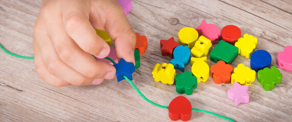 Preschooler making bracelet from thread and wooden colored beads. Development of kids motor skills, coordination and logical thinking