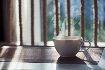 a morning hot coffee in white cup in sunshine scene with shade and white smoke from hot water