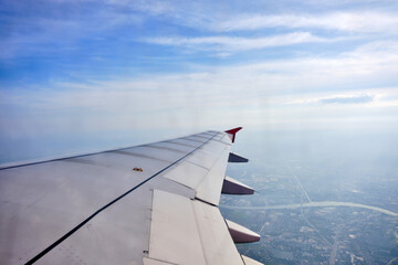 Fototapeta na wymiar a view from airplane window that has a wing with red winglet in the sky with cloud and city below