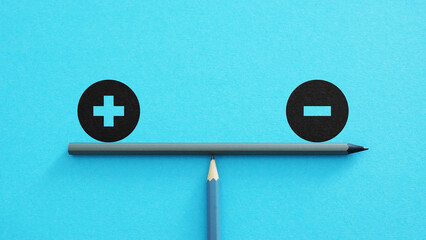Plus and minus or positive and negative symbols are in balance on a scales with blue background....