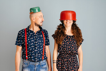 Quirky Couple With Colorful Pots on Their Heads Standing Against a Gray Background