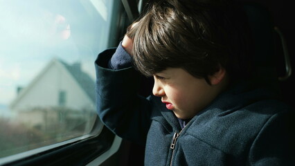 One small boy seated by train window looking at landscape scenery pass by while squinting his eyes...