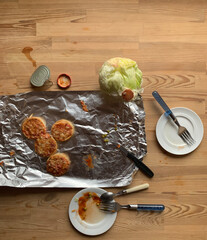 There are dirty dishes on the old kitchen wooden table after eating. Foil, iceberg cabbage, two...