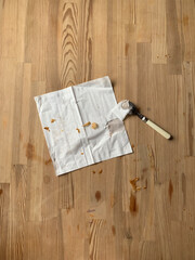 Dirty white square paper napkin with crumbs and a teaspoon on a dirty kitchen wooden table.