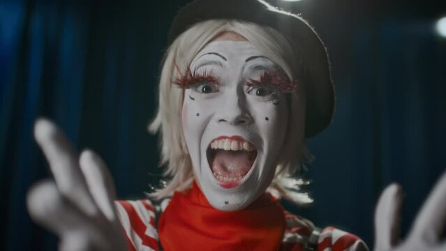 Cheerful female mime artist standing on theatre stage, looking at camera, yelling in excitement, dancing and showing thumbs up during comedy show