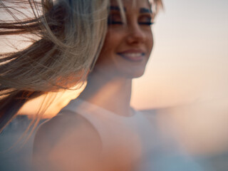 The setting sun casts a golden light on a woman's profile, her hair flowing in the seaside breeze