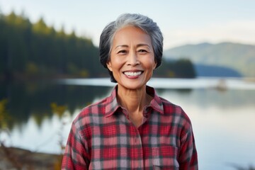 Portrait of a grinning asian woman in her 50s wearing a comfy flannel shirt isolated in serene...