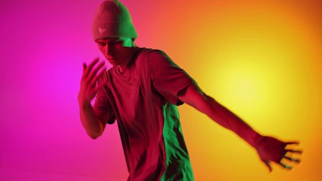 Talented dancer dressed streetwear performing freestyle moves in motion in neon light against gradient pink-yellow background. Concept of art, hobby, sport, creativity, fashion and style, action. Ad