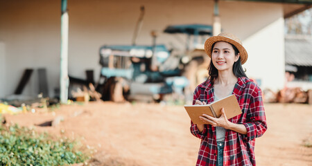 Optimistic young farmer holding a notepad stands in front of farm equipment, ready to tackle the...