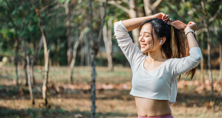 Joyful woman ties her hair, smiling with closed eyes, wearing a cropped white top and pink leggings...