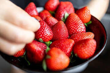 Juicy, sweet, ripe, fresh strawberries in a plate. A handful of strawberries in a saucer. The girl...