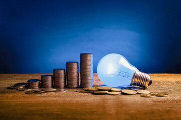 Lying illuminated light bulb next to stacks of coins