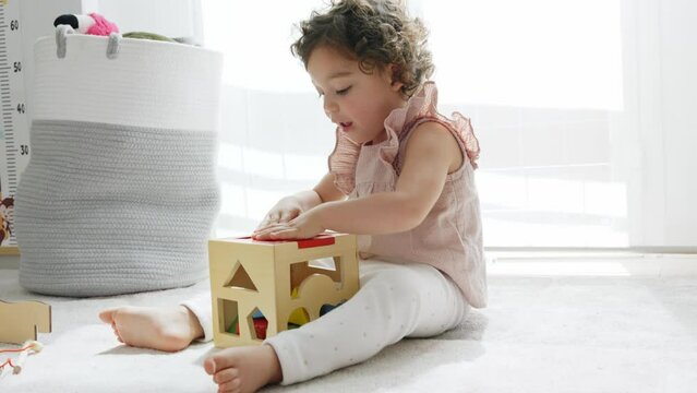 4k slow motion horizontal video of a little girl sitting on the floor playing with a cube of colorful wooden pieces and shapes. montessori materials. concept development and learning in the childhood
