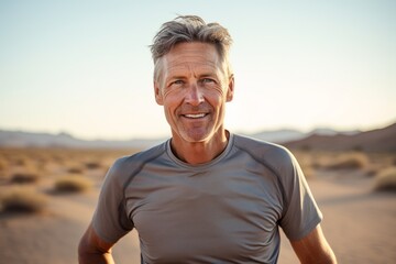 Portrait of a jovial man in his 50s wearing a moisture-wicking running shirt while standing against backdrop of desert dunes