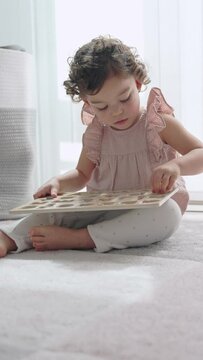 video 4k of a little girl with curly hair playing sitting on the carpet in her room with a wooden alphabet, Montessori material. concept development and learning in the childhood stage.